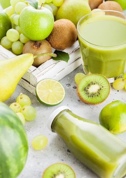 Vidrio y una botella de batido fresco con frutas en tonos verdes orgánicos en caja blanca vintage en cocina de piedra. Pera y uvas con kiwi y lima con manzana.