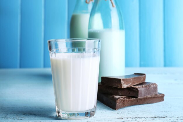 Vidrio y botellas de leche con trozos de chocolate sobre fondo de tablones de madera de color