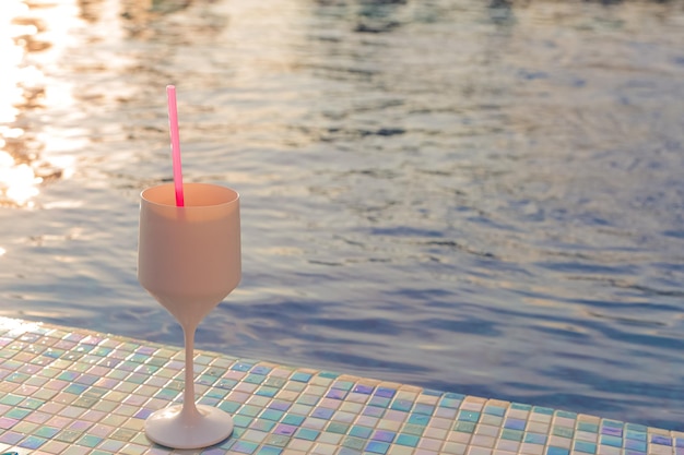 Vidrio con un cóctel se encuentra al lado de la piscina en los rayos del sol poniente