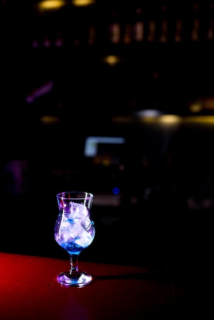 Vidrio con hielo y jarabe azul de pie en el bar en un restaurante de pub discoteca fondo oscuro