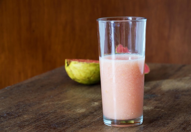 Foto vidrio transparente con jugo de guayaba y parte de guayaba dividida en el fondo fuera de foco