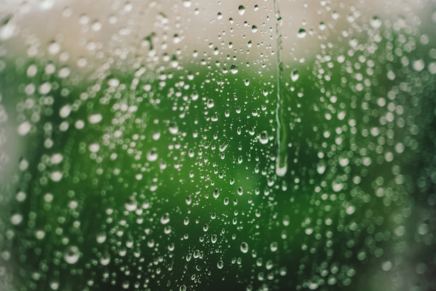 Vidrio de ventana con gotas de lluvia. Fondo verde atmosférico con gotas de lluvia en bokeh. Gotas de cerca. Textura transparente detallada en macro con espacio de copia. Clima lluvioso. Concepto de aislamiento.