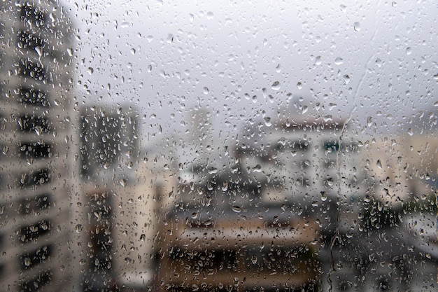 vidrio de ventana con gotas de lluvia que muestran la ciudad borrosa en el fondo