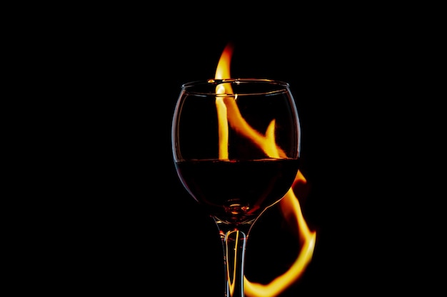 Vidrio con vino en llamas y llamas sobre un aislamiento de fondo negro