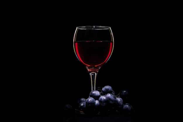 Vidrio con vino y uvas sobre un fondo negro