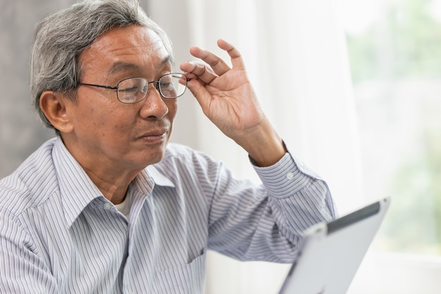 Vidrios asiáticos viejo anciano feliz usando mirando la pantalla de la tableta a la comunicación con el otro.