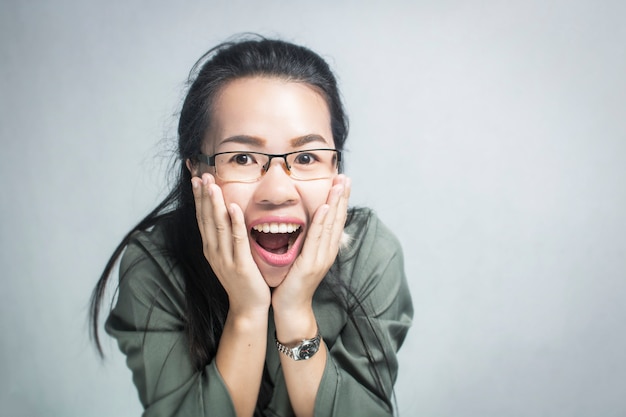 Vidrios que llevan de la mujer asiática sorprendida y feliz en fondo gris