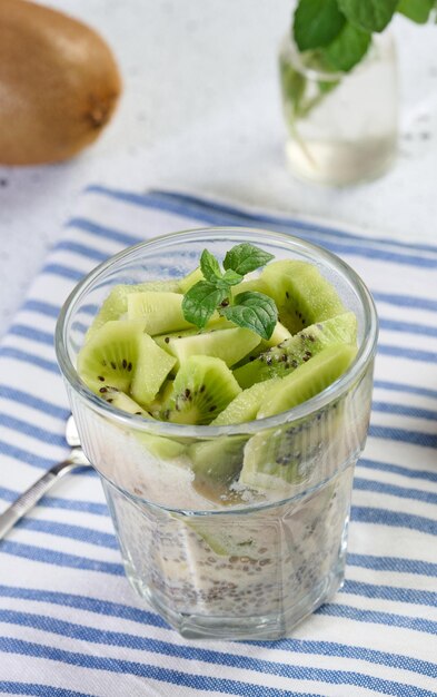 Vidro com sobremesa de chia e iogurte adornado com fatias frescas de kiwi em mesa branca