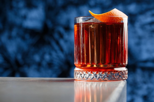 Vidro de cristal com coquetel alcoólico frio brilhante decorado com raspas de laranja Coquetel Negroni de fundo desfocado