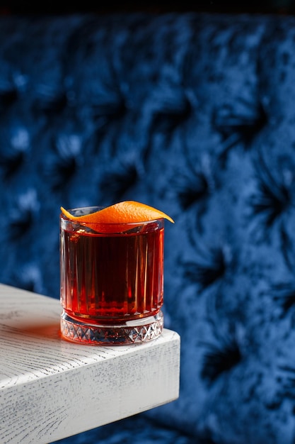 Vidro de cristal com coquetel alcoólico frio brilhante decorado com raspas de laranja Coquetel Negroni de fundo desfocado
