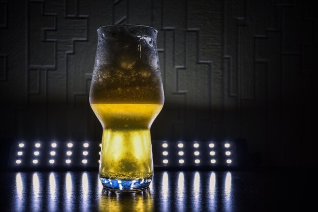 Foto vidro destacado com closeup de cerveja no escuro sobre a mesa vidro encaracolado com closeup de líquido amarelo