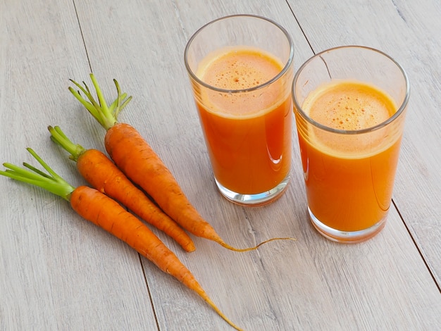 Vidro do suco de cenoura fresco com os vegetais no fundo de madeira.