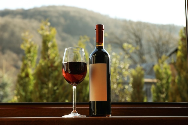 Vidro e garrafa de vinho fica no parapeito de madeira