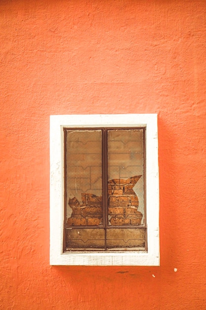 Vidro quebrado na janela na parede de cimento de gesso de cor laranja com janela de revestimento de moldura branca. Janela quebrada ou rachada.