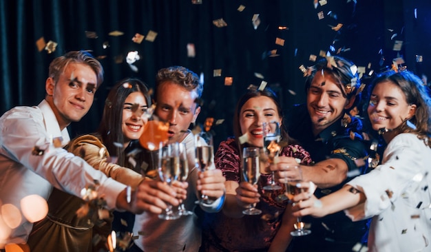 Vidros batendo. Grupo de amigos alegres comemorando o ano novo dentro de casa com bebidas nas mãos.