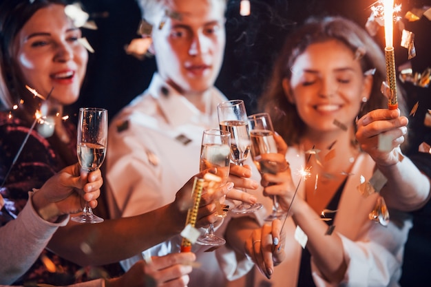 Vidros batendo. Grupo de amigos alegres comemorando o ano novo dentro de casa com bebidas nas mãos.