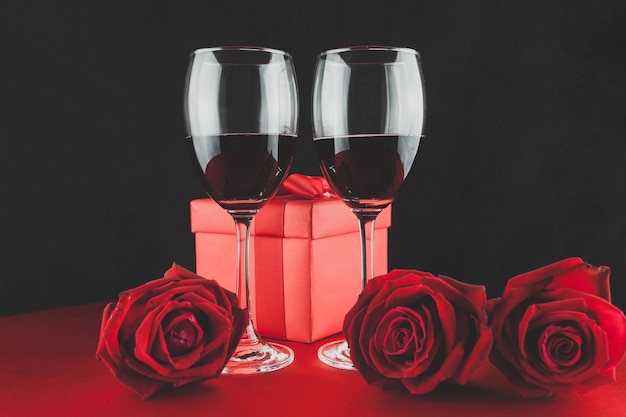 Vidros com vinho vermelho com um presente e três rosas