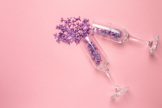 Vidros de champagne com as flores lilás no estilo mínimo do papel cor-de-rosa da cor. férias de verâo.