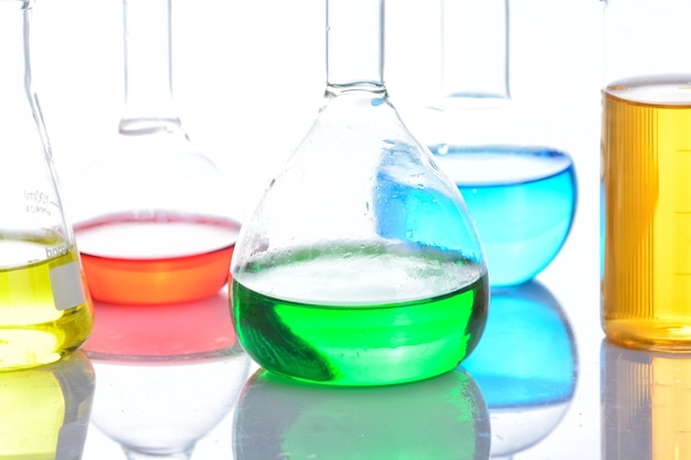 Vidros de laboratório com líquidos coloridos sobre mesa reflexiva sobre branco