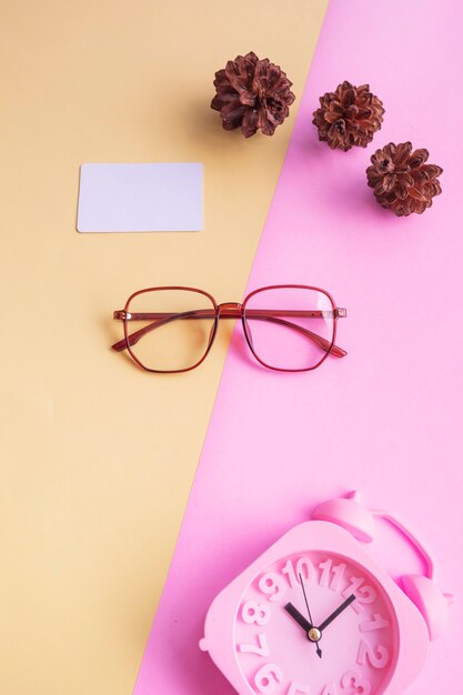 Vidros pentagonais na foto em estilo minimalista de verão em um fundo rosa pastel e amarelo. Despertador, flores de pinheiro, cartões de visita