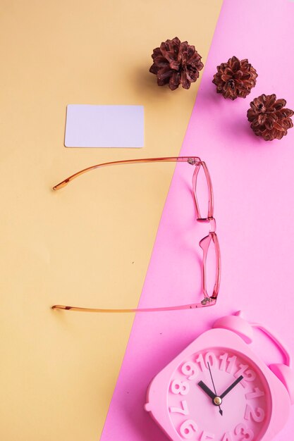 Vidros pentagonais na foto em estilo minimalista de verão em um fundo rosa pastel e amarelo. Despertador, flores de pinheiro, cartões de visita