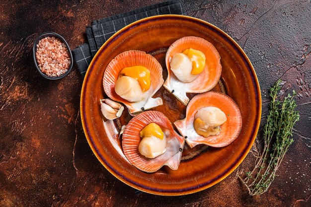 Vieiras crudas de mariscos en un plato rústico con tomillo. Fondo oscuro. Vista superior.