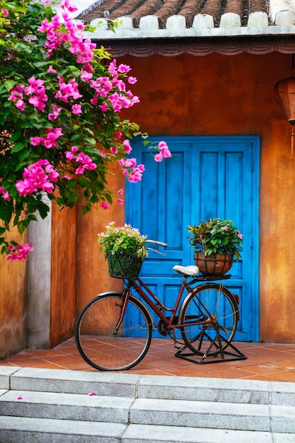 Una vieja bicicleta con flores en una canasta en el fondo de una vieja pared .Jardín decoración del hogar.Una vieja bicicleta contra la pared en el jardín.Vietnam