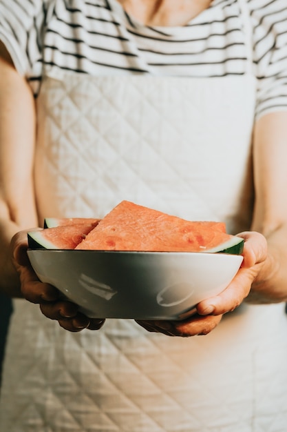 Vieja camarera ofrece y sostiene una sandía en un plato, frutas, vida sana, buena alimentación, conceptos mediterráneos, espacio de copia, imagen vertical, comida de verano y frutas refrescantes