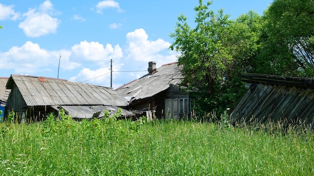 Una vieja casa abandonada y en ruinas con un granero de madera caído, cubierto de hierba, en el pueblo.