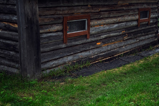 Una vieja casa de madera con rejas de metal en ventanas pequeñas. De cerca. Prisión domiciliaria.