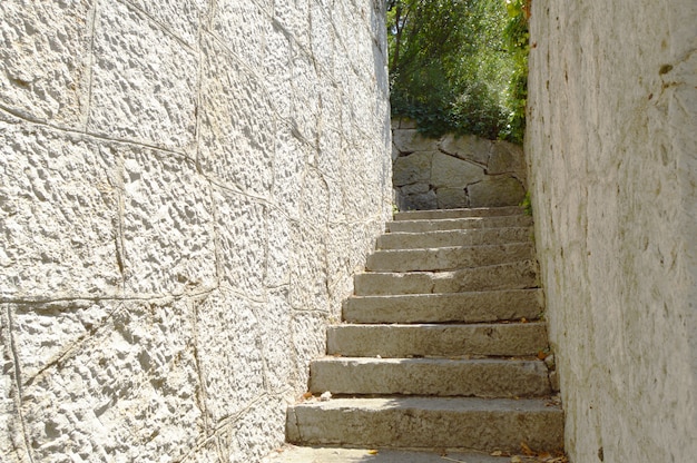 Vieja escalera estrecha con muro de piedra en ambos lados, que conduce hacia arriba, iluminada por la luz solar