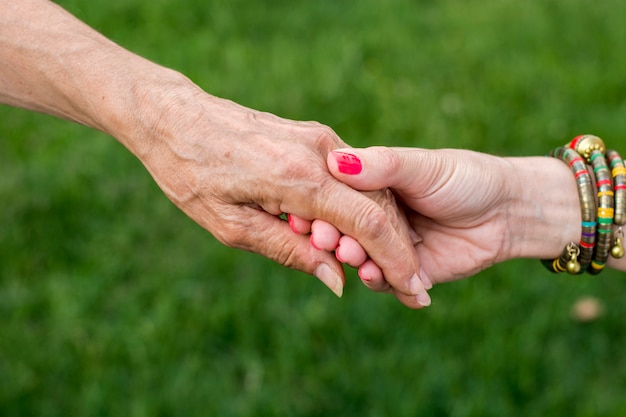 Vieja y joven mujer cogidos de la mano sobre fondo verde, primer plano