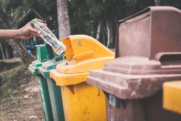 Vieja mano masculina tirando botella de plástico vacía en la basura