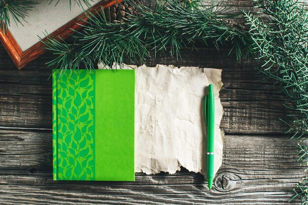 En la vieja mesa de madera están los elementos de la víspera de Navidad y año nuevo, cuaderno, bolígrafo, rama de un árbol