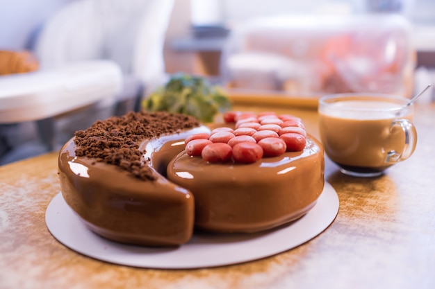 En una vieja mesa de madera hay un hermoso pastel de mousse de chocolate con una taza grande transparente con café aromático y planta de interior.