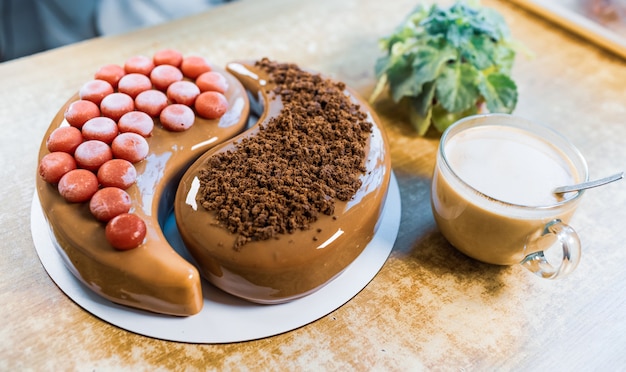 En una vieja mesa de madera hay un hermoso pastel de mousse de chocolate con una taza grande transparente con café aromático y planta de interior.