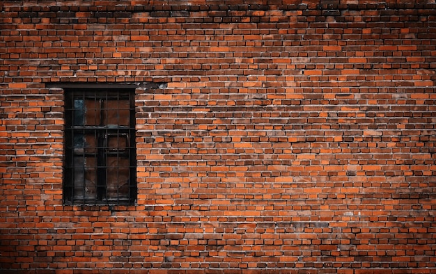 Vieja pared de ladrillo negro y ventana cerrada con barras de metal