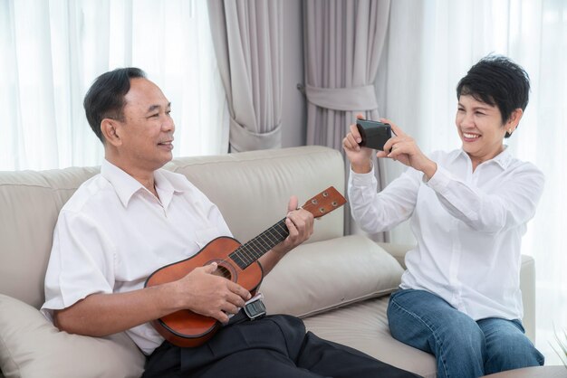 Foto una vieja pareja asiática canta una canción con alegría y emoción y toca el ukelele juntos en la sala de estar de su casa.