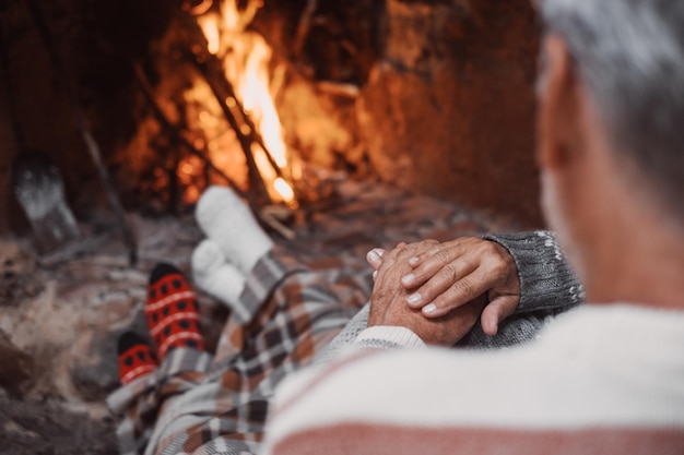 Vieja pareja caucásica pasando tiempo libre juntos en casa Amante y romántico esposo y esposa relajándose mientras se toman de la mano frente a la chimenea ardiente durante las vacaciones de Navidad de invierno