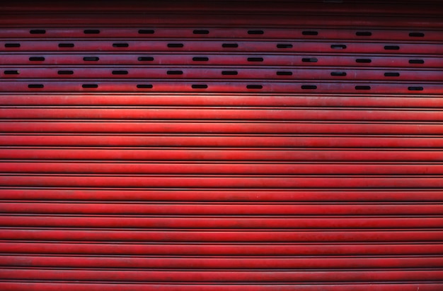 La vieja puerta del obturador del rodillo del metal de la aleación texturizada roja envejecida detallada del vintage, almacena el diseño exterior delantero usado en sector de la construcción como material de construcción.