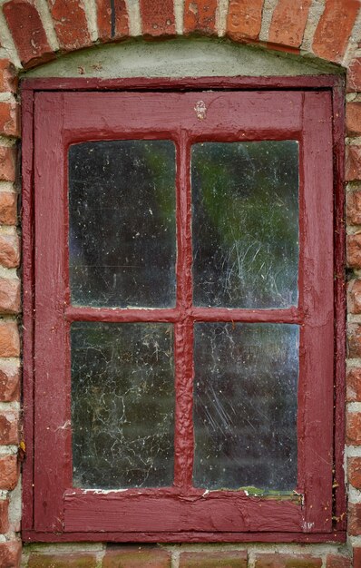 Vieja ventana sucia de una casa o casa de paredes de ladrillo Antiguo marco con marco de metal rojo en un edificio histórico con una textura de pintura grumosa Detalles exteriores de un alféizar en una ciudad rural tradicional