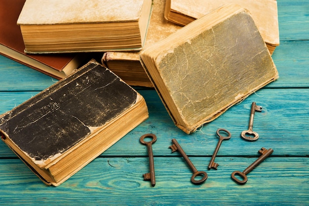 Viejas llaves y pila de libros antiguos sobre fondo de madera azul