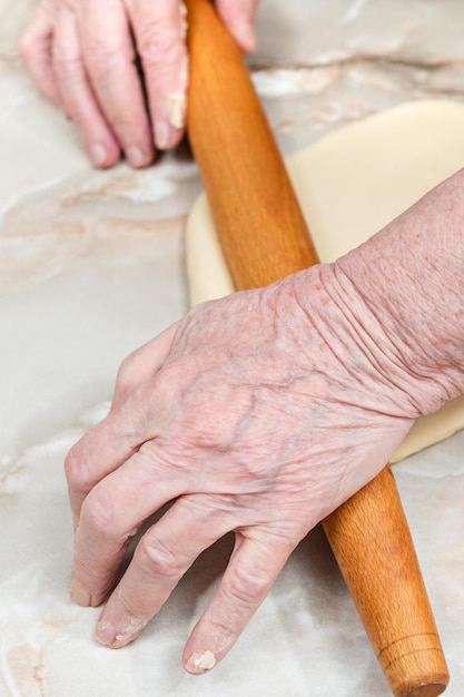 Viejas manos con un rodillo extienden la masa sobre la mesa