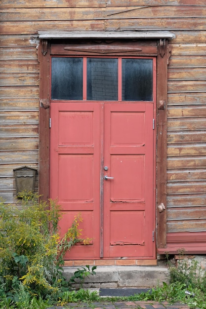 Viejas puertas de madera roja entrada a la casa de madera con pintura desconchada marchita en las paredes Tartu Estonia