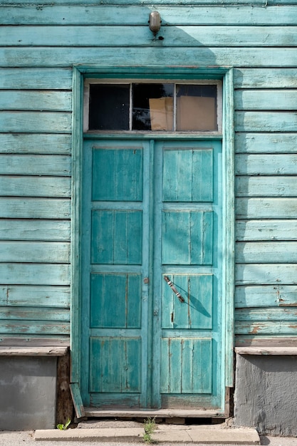 Viejas puertas de madera turquesa entrada a la casa de madera con pintura marrón pelada marchita en las paredes en Tartu Estonia