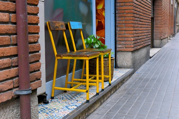 Las viejas sillas amarillas están cerca del edificio de ladrillo naranja a lo largo del pavimento de piedra en un día nublado.