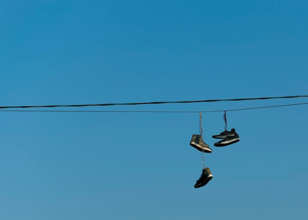 Viejas zapatillas rotas cuelgan de cables eléctricos contra el cielo azul de la ciudad