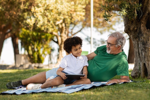 El viejo abuelo europeo sonriente y el niño de raza mixta se divierten en el parque disfrutan del tiempo libre