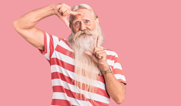 Viejo anciano con cabello gris y barba larga con camiseta a rayas sonriendo haciendo marco con manos y dedos con cara feliz creatividad y concepto de fotografía