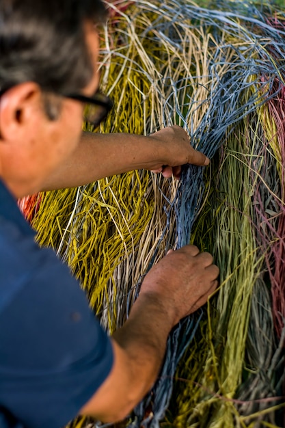 Foto viejo artesano latinoamericano tejiendo con sus manos mostrando sus herramientas y materiales